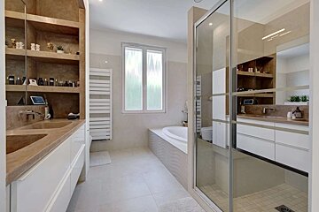 Sleek, modern bathroom with double vanity, integrated shelves, bathtub, and walk-in shower. Light colors, large window.