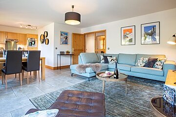 Bright, open-plan living room featuring a light-blue sectional sofa, a coffee table, and an adjacent dining area.