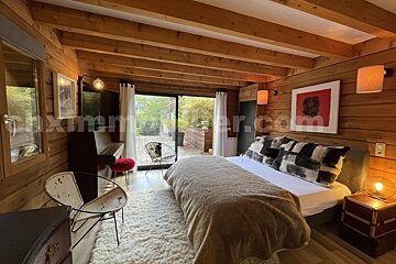 A warm, rustic bedroom with exposed wooden beams, a large bed on a fluffy rug, and sliding doors opening to an outdoor deck.