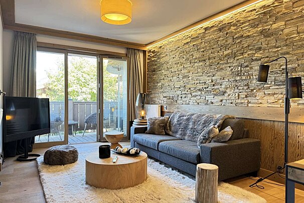 Cozy living room with a stone accent wall, gray sofa, wooden coffee table, fluffy white rug, and sliding doors to a balcony.
