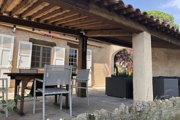 A patio with a table and chairs under a wooden roof