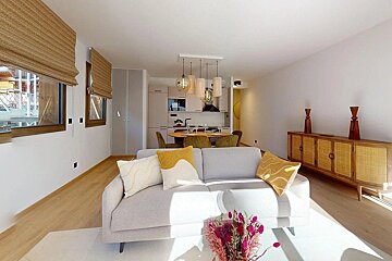 Bright, open-plan living/dining/kitchen with a light gray sofa, yellow cushions, and wood dining set. A modern kitchen and wood/rattan sideboard complete the contemporary, natural-toned space.