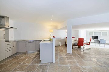 An open-plan living space with a modern kitchen featuring grey cabinets, a dining area with red chairs, and a lounge, all on a tiled floor.
