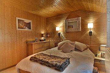 Cozy, rustic cabin bedroom with wood-paneled walls, a bed topped with a faux fur throw, and warm lighting from wall lamps.