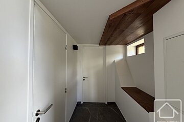A minimalist white hallway with a dark tile floor, wooden ceiling accents, closed white doors, and a small window.