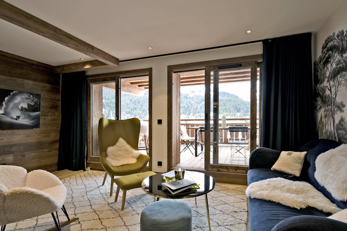 Stylish, cozy living room with rustic wood walls, plush furniture, a large mountain-view balcony, and a monochrome tree mural.