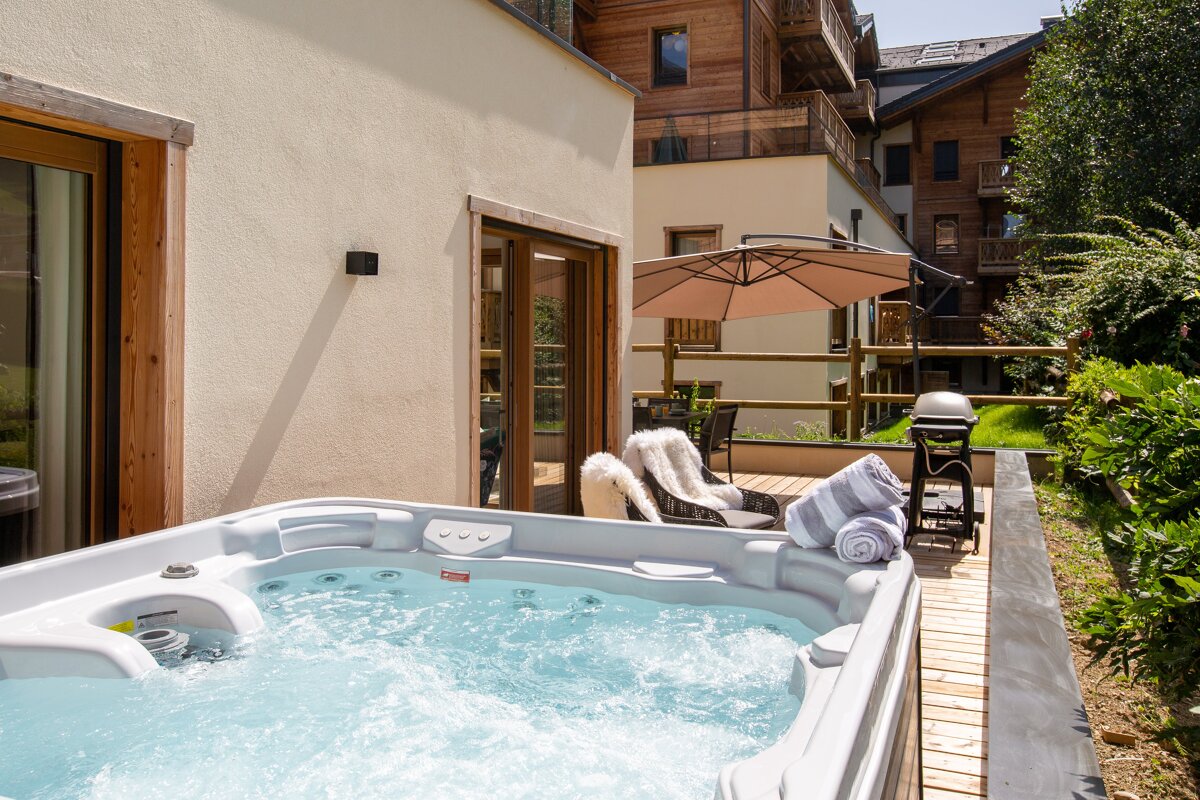 A hot tub sits on a wooden deck in front of a house