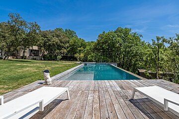 A large swimming pool is surrounded by trees and a wooden deck