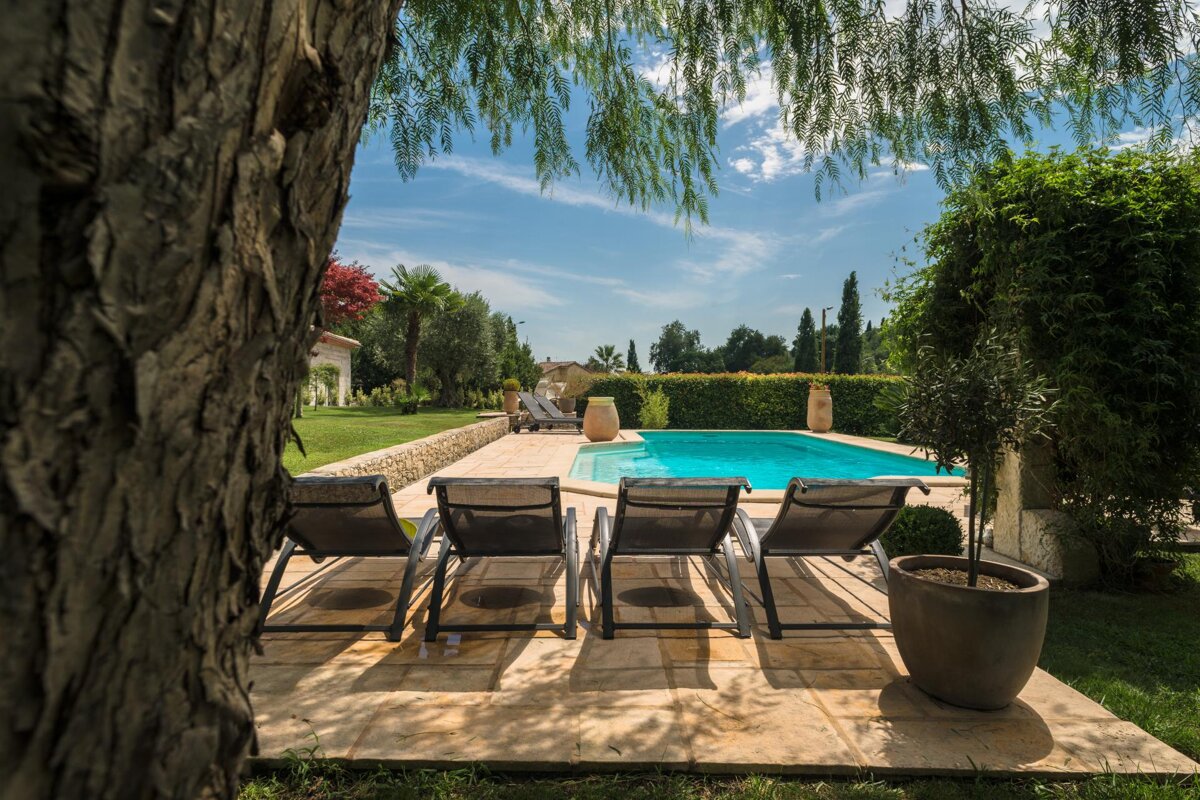 A swimming pool is surrounded by chairs and a tree