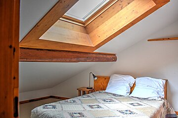 Cozy attic bedroom featuring a bed with a patchwork quilt under a slanted ceiling with a large wooden skylight.