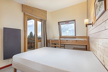 A cozy bedroom featuring a white mattress, wooden bunk beds, a balcony door, a small window, and wood-paneled walls with a wall heater.