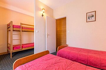 A bedroom with two single beds with pink covers in the foreground and a wooden bunk bed visible behind a partition wall.