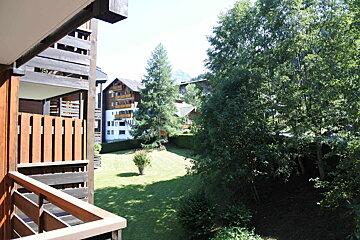 A balcony overlooking a lush green field with trees and buildings in the background