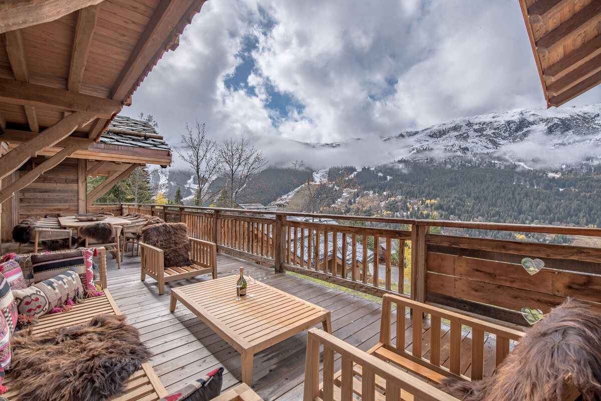 A bottle of wine sits on a wooden table on a balcony overlooking mountains