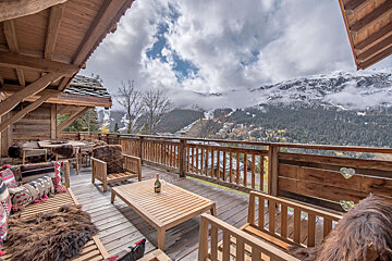 A bottle of wine sits on a wooden table on a balcony overlooking mountains