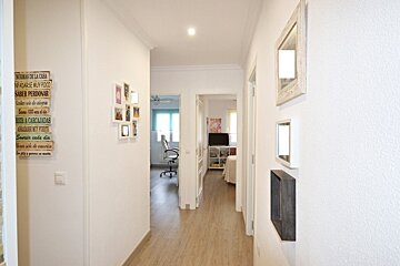 Bright white hallway with light wooden floors, decorated walls, and open doorways leading to other rooms in the background.