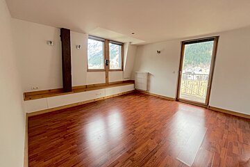 Empty room with glossy wood floors, white walls, a built-in bench, and windows/balcony doors offering mountain and valley views.