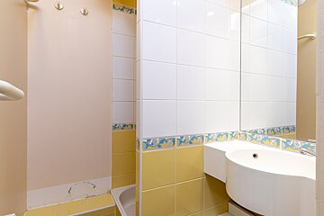 Bright bathroom with white sink, mirror, and tub. Features yellow & white tiles with a decorative border and a light pink wall.
