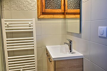 Modern bathroom with white tiled walls, wooden vanity, sink, chrome faucet, mirror, rustic wooden cabinet, and a white towel radiator.