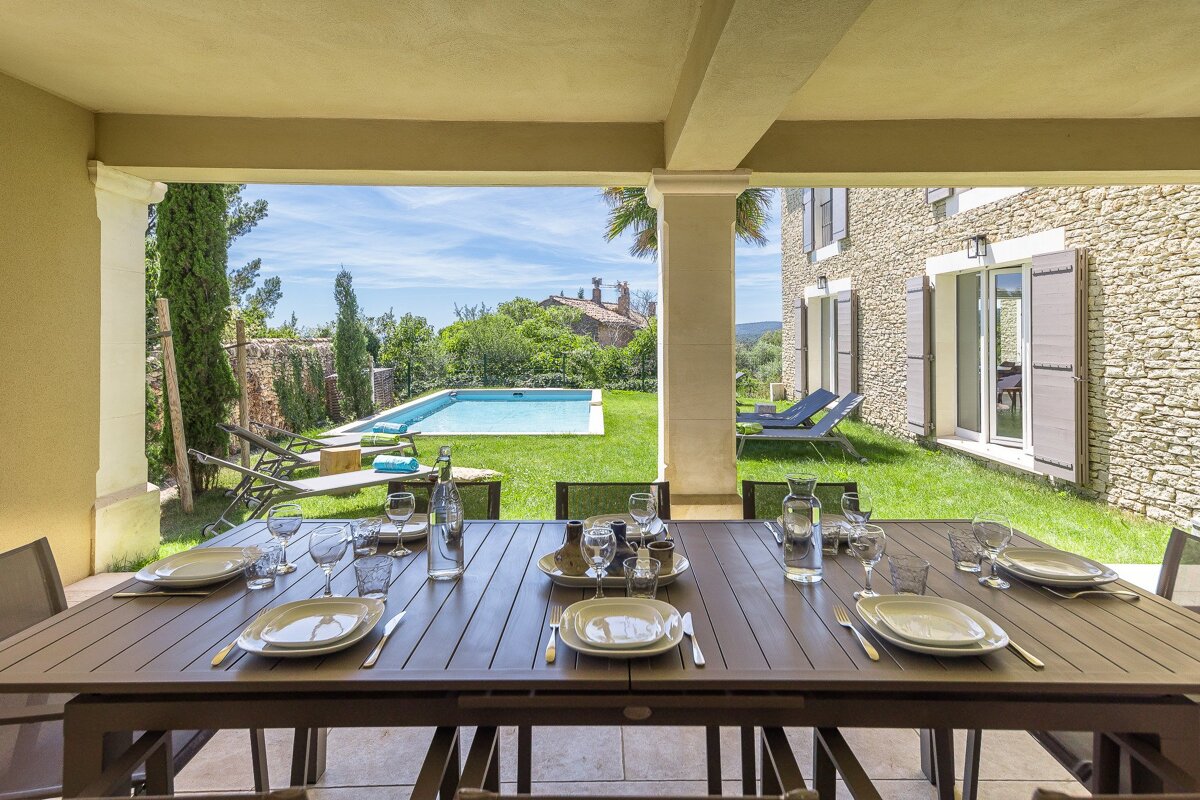 A patio with a table and chairs and a pool in the background