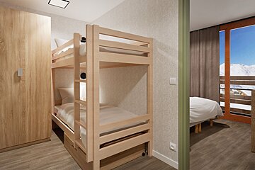 A modern room with light wood bunk beds, a wardrobe, and a peek into another room with a bed and a balcony showing snowy mountains.