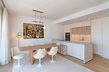 A modern open-concept kitchen and dining room featuring sleek white cabinets, a light wood table, stylish chairs, and vibrant abstract artwork.
