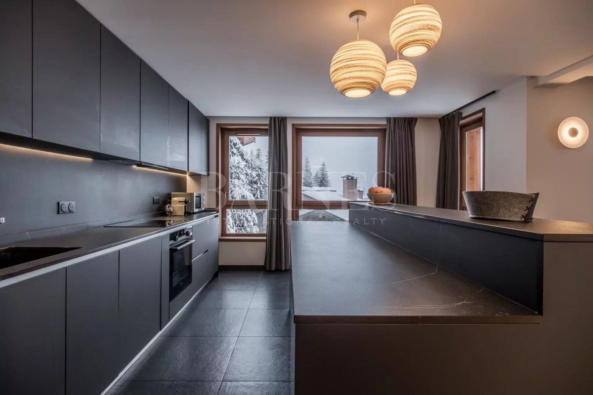 Modern dark gray kitchen with under-cabinet lighting, an island, and large windows revealing a snowy winter landscape.