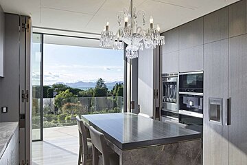 Luxurious modern kitchen with a crystal chandelier, island, and large windows opening to a stunning ocean and mountain view.