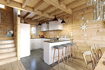 A rustic log cabin interior with modern white kitchen, breakfast bar, wooden stairs, and star decorations on plank walls and ceiling.