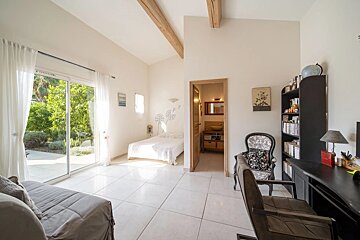 A bright bedroom featuring a desk, a sliding glass door opening to a garden, and an adjacent bathroom.