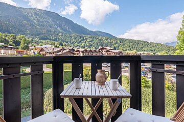 A balcony with a table and chairs and mountains in the background