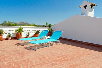 Two blue lounge chairs sit on a rooftop with potted plants