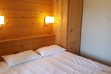 A bedroom with wood paneling and a bed with white sheets