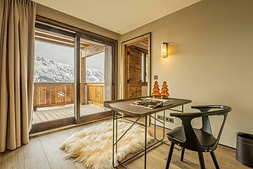 Cozy cabin study with a desk, black chair, and fluffy rug, featuring sliding glass doors with a view of snowy mountains.