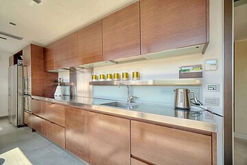 A modern kitchen features warm wooden cabinets, stainless steel countertops and backsplash, an integrated sink, a kettle, and built-in appliances.