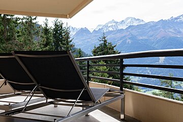 Two lounge chairs on a balcony with mountains in the background