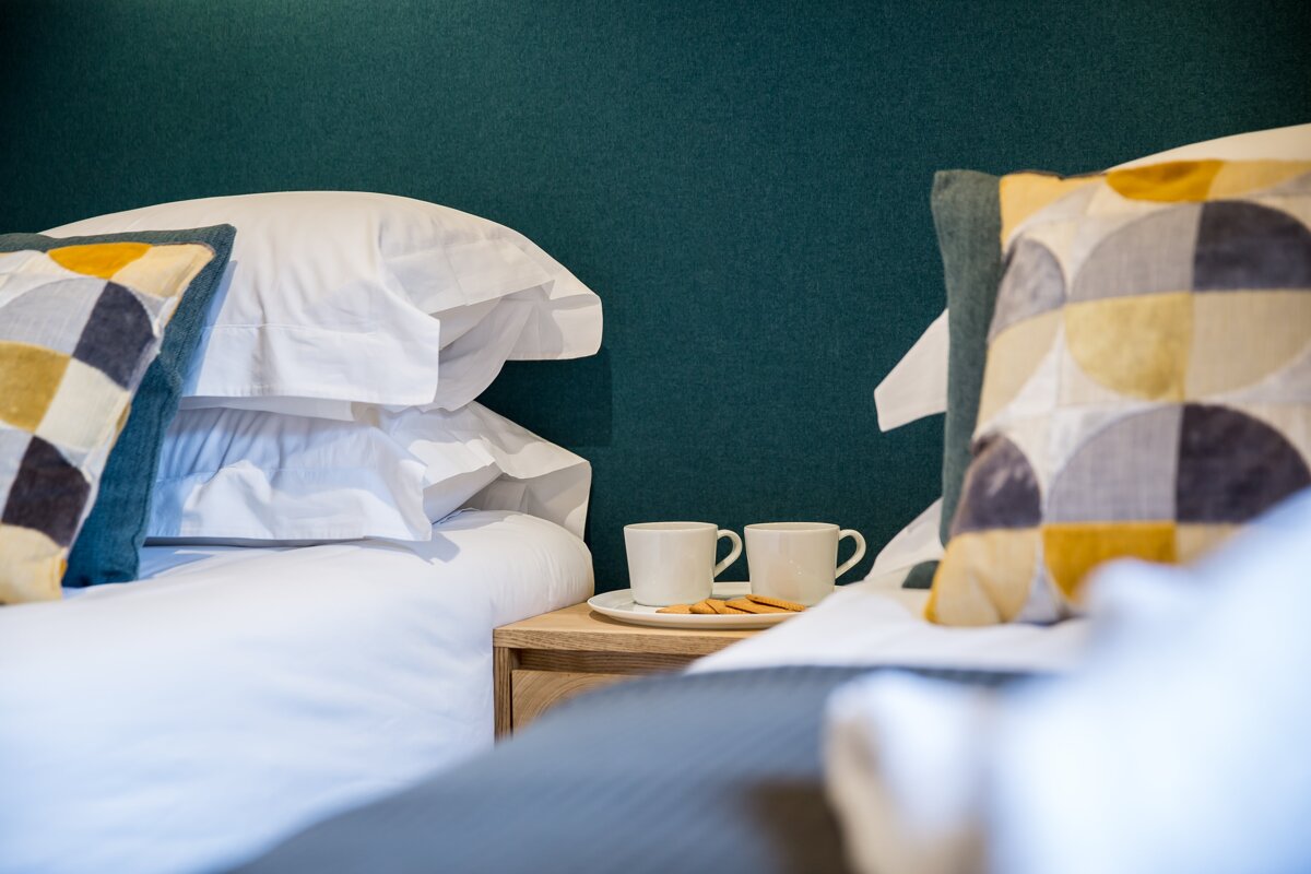 Two cups of coffee sit on a nightstand next to a bed