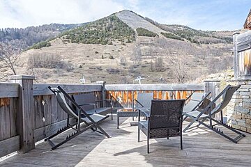 A deck with chairs and a table with a mountain in the background