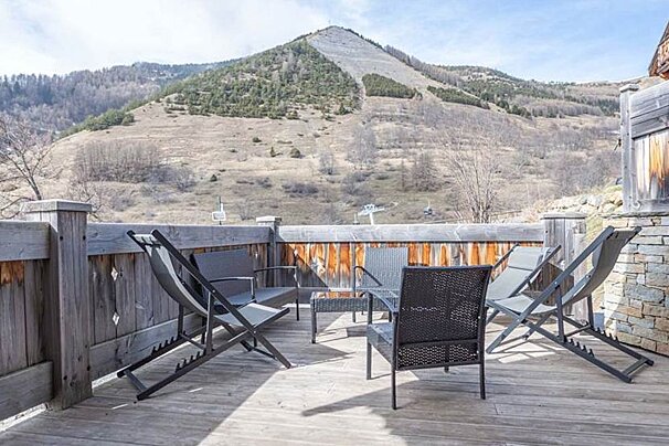 A deck with chairs and a table with a mountain in the background