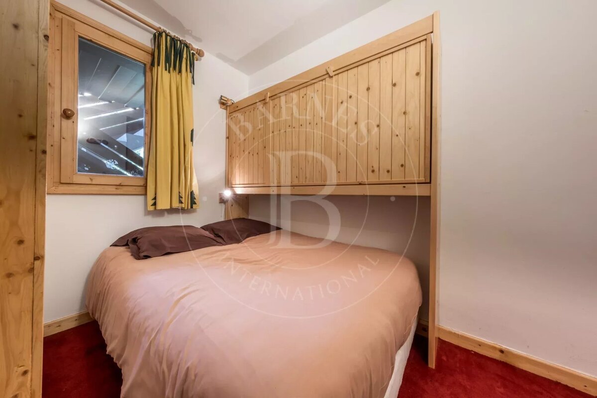 A cozy bedroom with a bed featuring a light pink duvet and brown pillows, a wooden headboard, a window with a yellow curtain, and red carpet.