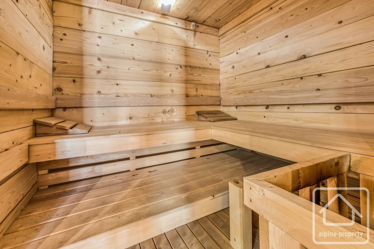 A clean, empty sauna room made of light wooden panels, featuring multi-level benches and a slatted floor.