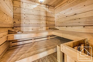 A clean, modern wooden sauna interior features multi-level benches, light wood paneling, and a slatted floor.