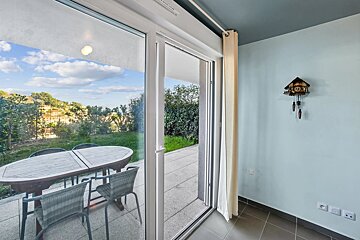 View through sliding glass doors to a patio table and garden. Inside, a cuckoo clock hangs on a light blue wall.
