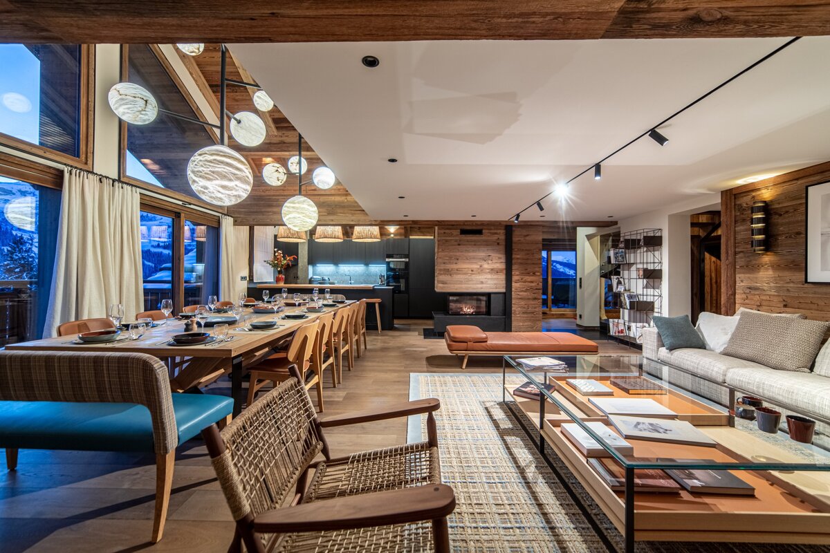 A spacious, modern alpine chalet with an open-plan living and dining area, cozy fireplace, and stunning snowy mountain views.