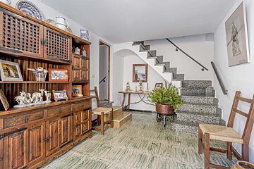 A cozy, rustic room features a large wooden hutch with decor, green patterned floor tiles, and a granite staircase. A potted fern and console table are under the stairs.