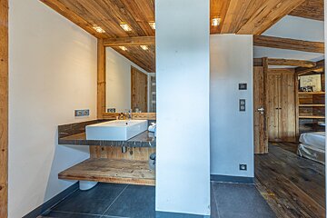 Modern bathroom with a wooden ceiling, floating sink vanity, and a white pillar next to a rustic hallway.