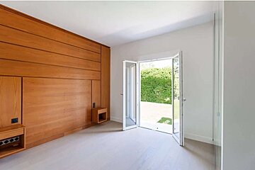 Modern room with warm wood paneling, light flooring, and open glass doors leading to a lush green garden.