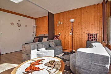 A sunlit living room with gray modular sofas, a unique round coffee table, and walls partially paneled in wood, creating a cozy yet modern space.