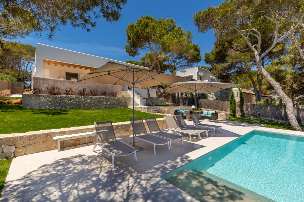 A swimming pool with chairs and umbrellas in front of a house