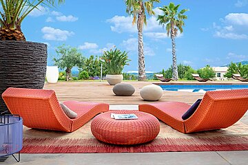 Two orange lounge chairs sit on a wooden deck near a swimming pool